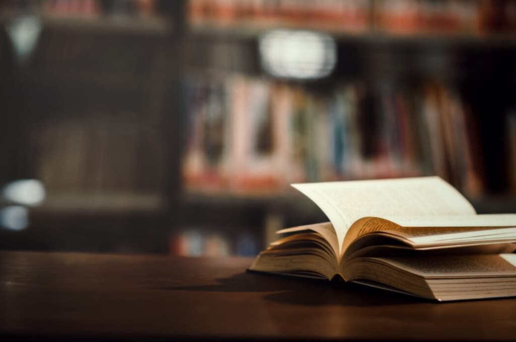 An open book on a table with a blurred bookshelf in the background