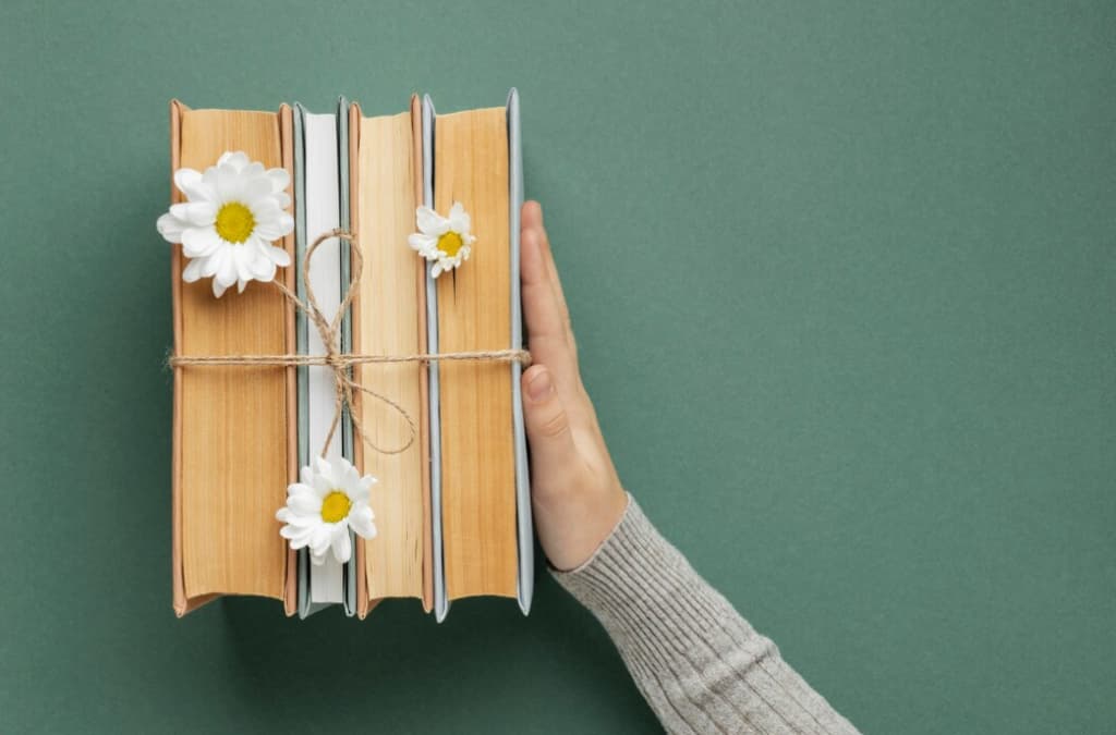 A hand holding a bundle of books tied with string and flowers on green background