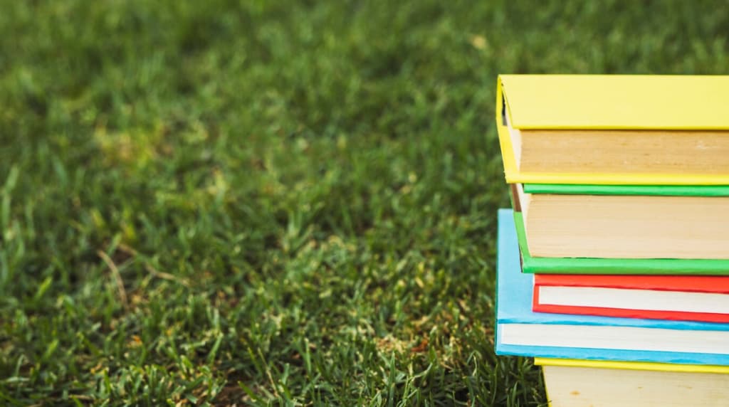 A stack of colorful books on a lush green lawn in daylight
